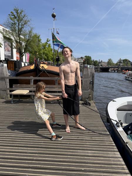 A young child playfully pulls a rope on a sunny day, with an older person smiling nearby on a wooden dock